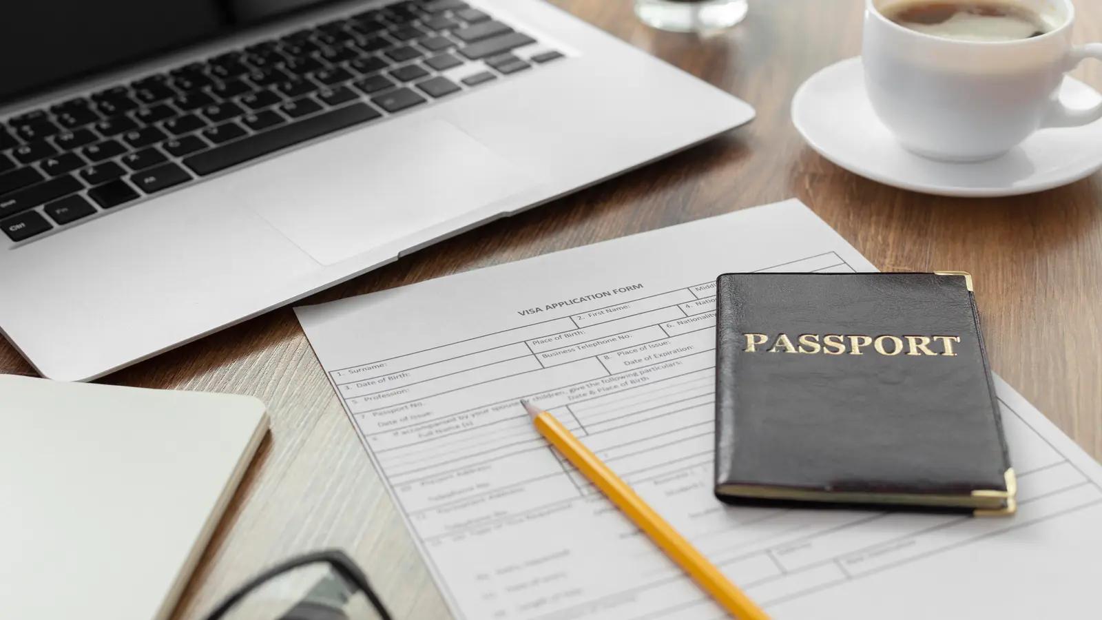 A passport on application forms beside a laptop