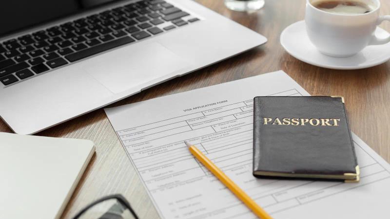 A passport on application forms beside a laptop