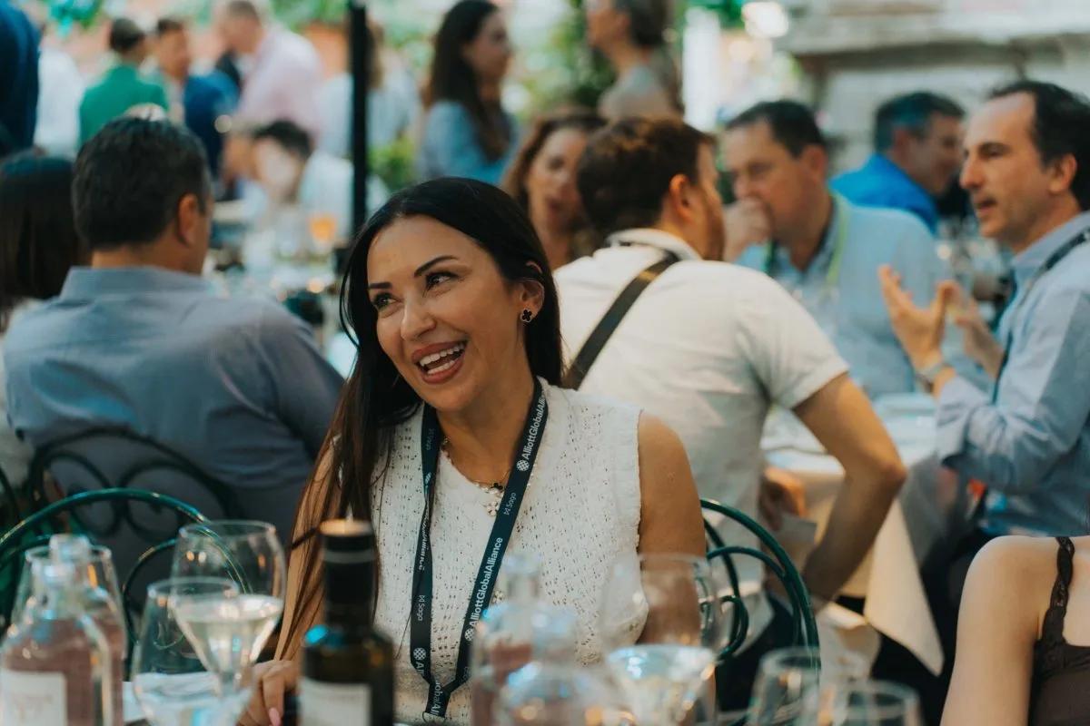 A delegate laughing in conversation at an outdoor conference dinner, wearing an Alliott Global Alliance lanyard