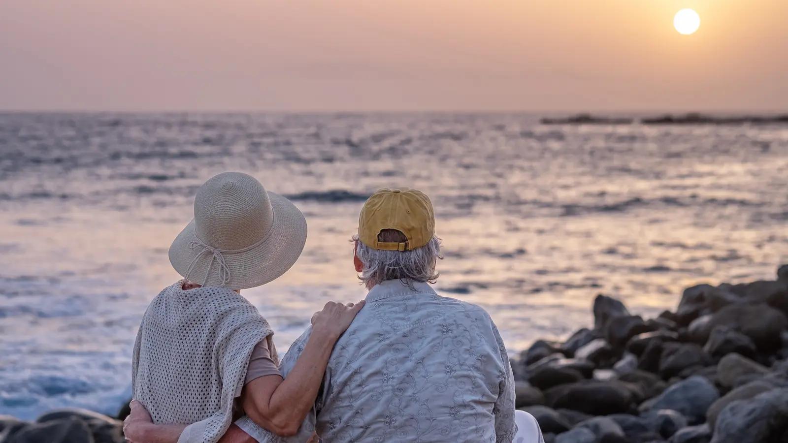 A senior couple sitting together by the sea at sunset