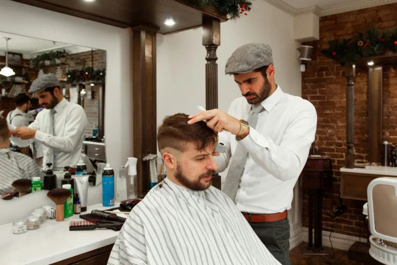 Barber w kaszkiecie układa włosy klienta w salonie