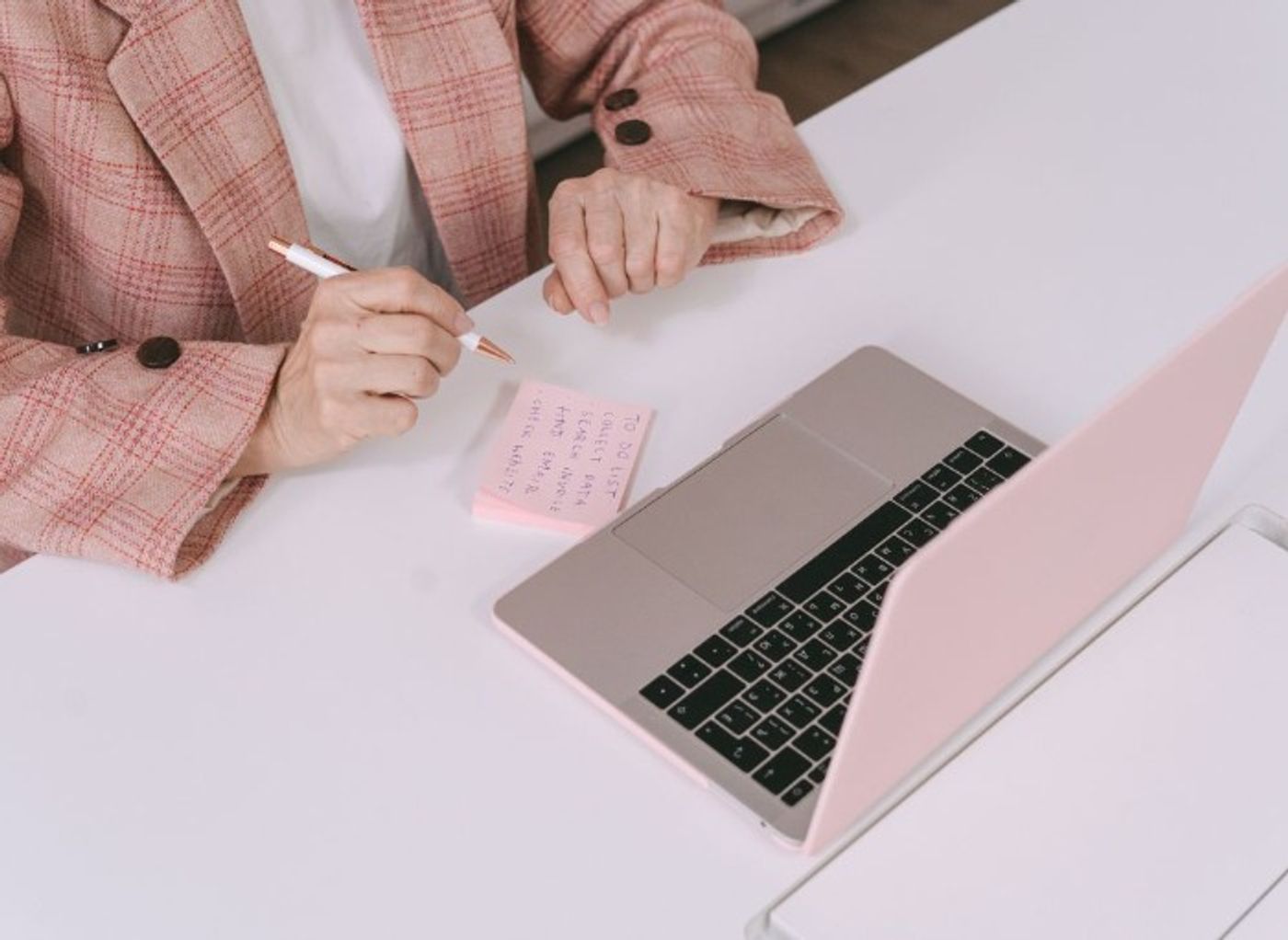 Woman in pink suit writing to-do list on pink post-it