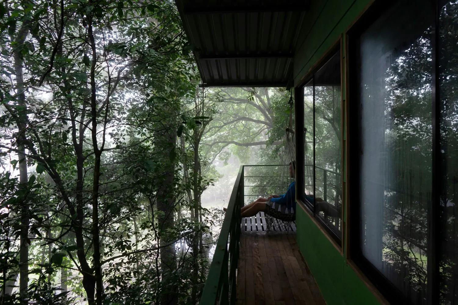 A person sites on a balcony looking out onto a forest