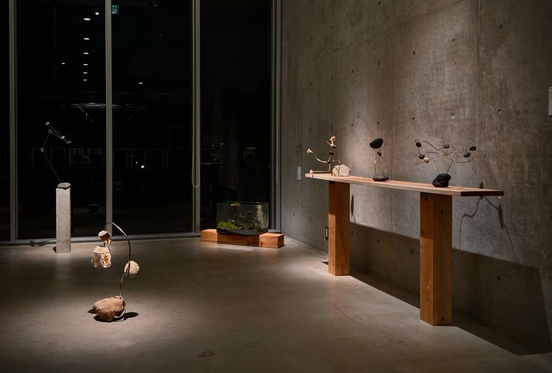    “いしの積み重ねとなるように”。　本作は千葉が展開する《wonder》シリーズの一環である。作家は数時間以上をかけて海や山へと赴き、産地や種類にこだわりながら自ら小石を採取し、自然の形をそのままに金属と組み合わせて構成している。 　 シリーズは「wonder_balance（制作番号）」と「wonder_unbalance（制作番号）」の二系統に分かれる。前者は、石同士が均衡を保つことで固定を必要とせずに成立する構造を指し、後者は、安定しない配置を都度固定することで成立する構造を意味している。なお、本作は《wonder_balance》に属し、展示に際しては安全性のため固定を施している。  　我々には測り得ない時間領域にある石が、緩やかに、さも楽しげに揺らぐ。まるで意志や感情を宿すかのように、それらは人の時間と響き合い、共に変化していく。そこには、自然と人間とが寄り添いながら紡ぎ出す、静かな対話の風景が広がっている。