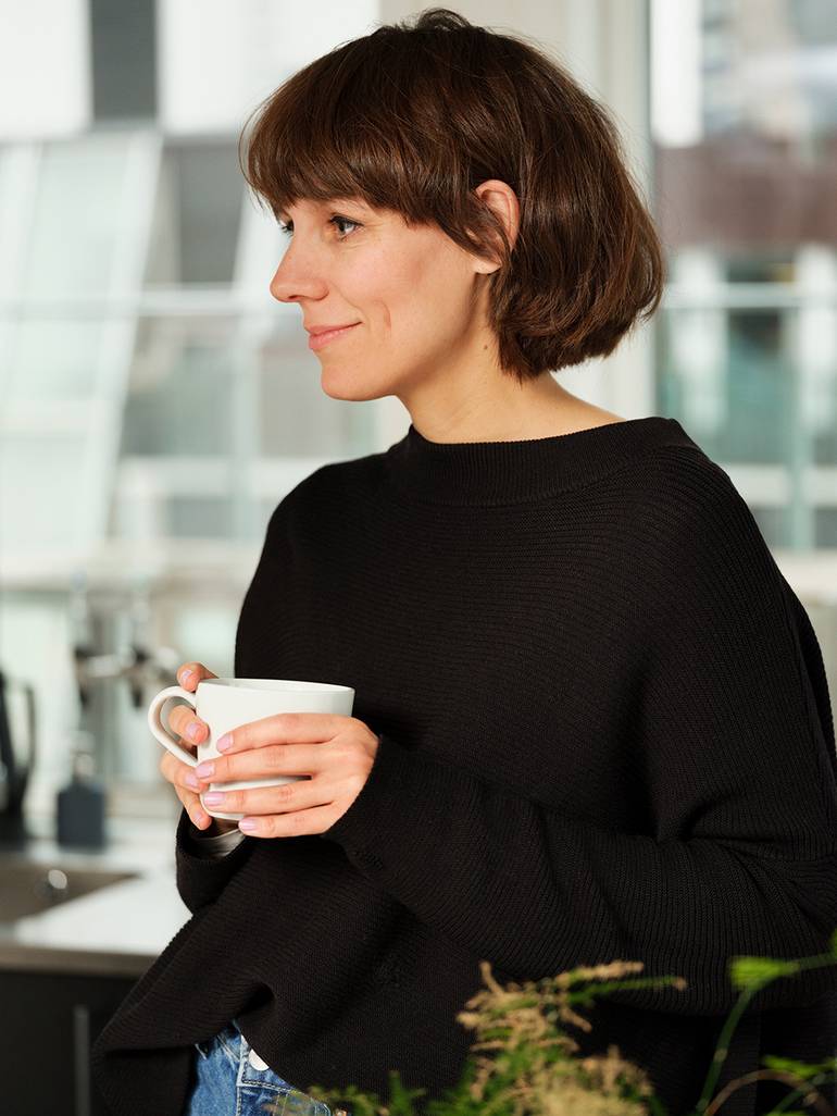 En dame står i et kontorlandskap, med en kaffekopp i hendene