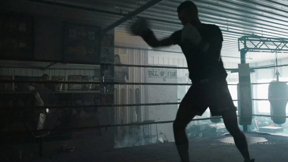 Charles Jourdain shadowboxes alone in a gritty boxing ring, light cutting through gym windows.