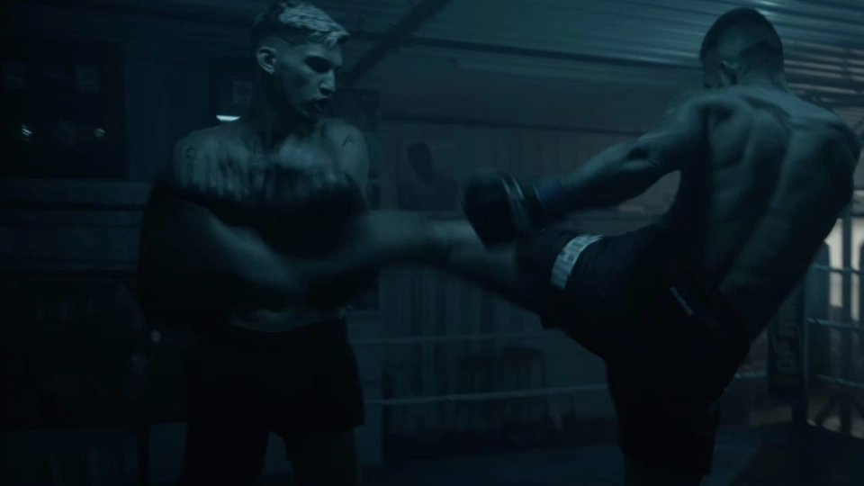 Two fighters mid-fight in a dimly lit gym, one delivering a powerful kick to the other's side during a UFC training session
