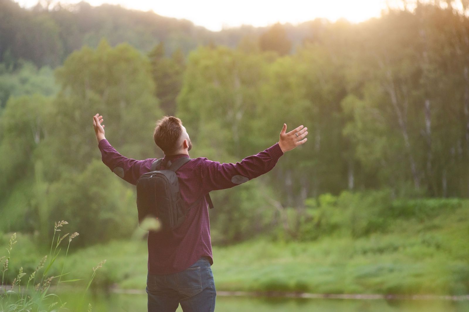 A man with arms raised toward the sunrise at the edge of a forest