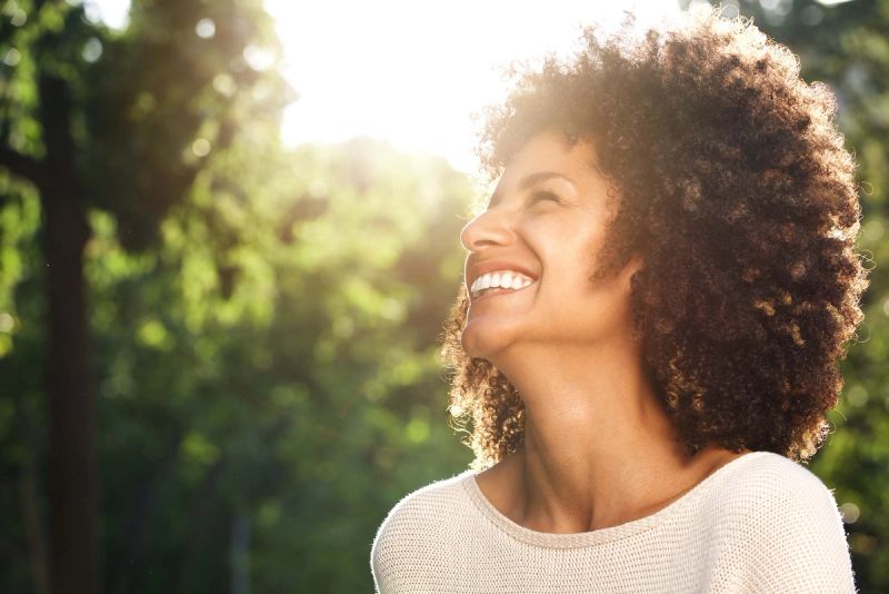 A woman smiling in the sunlight among trees