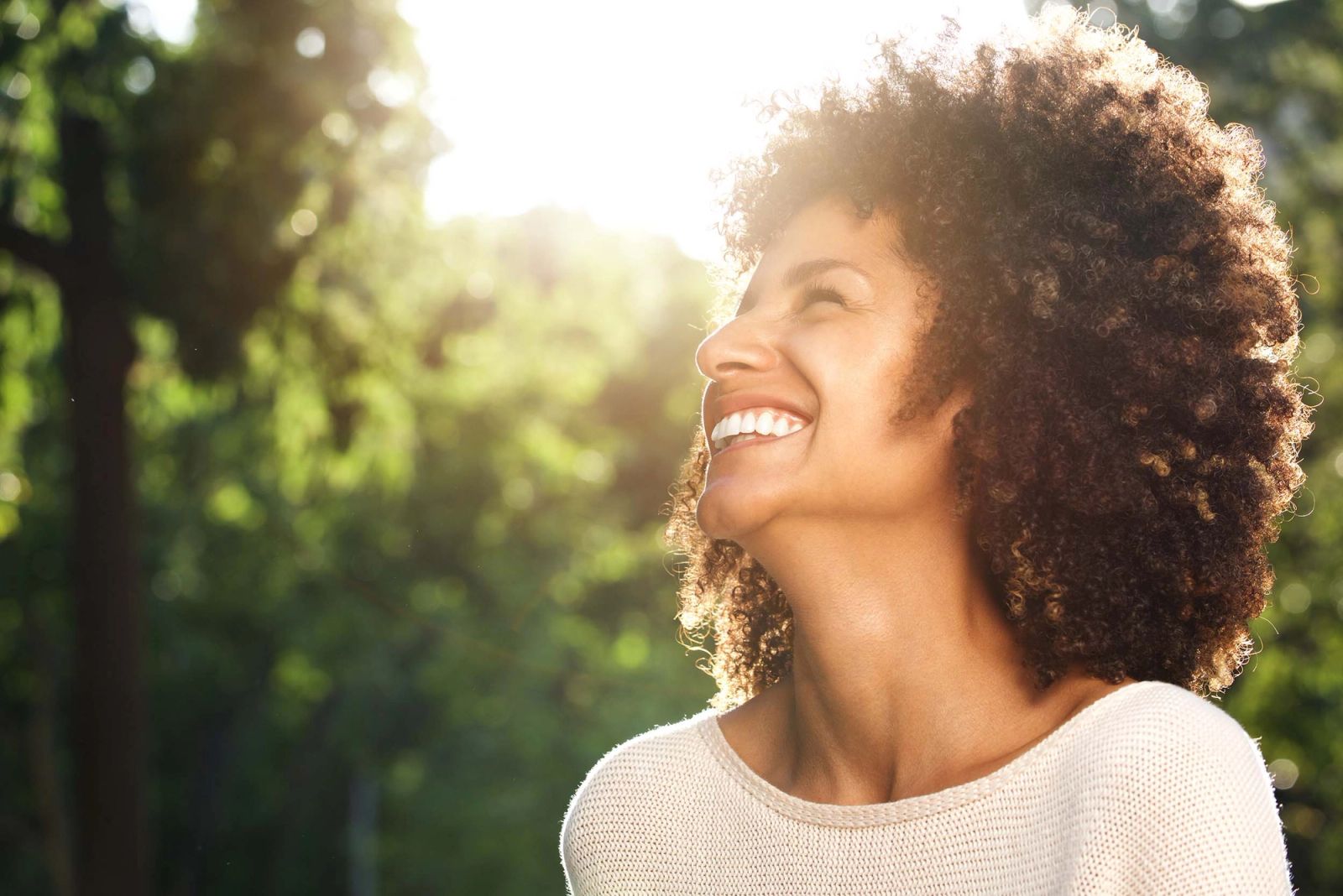 A woman smiling in the sunlight among trees