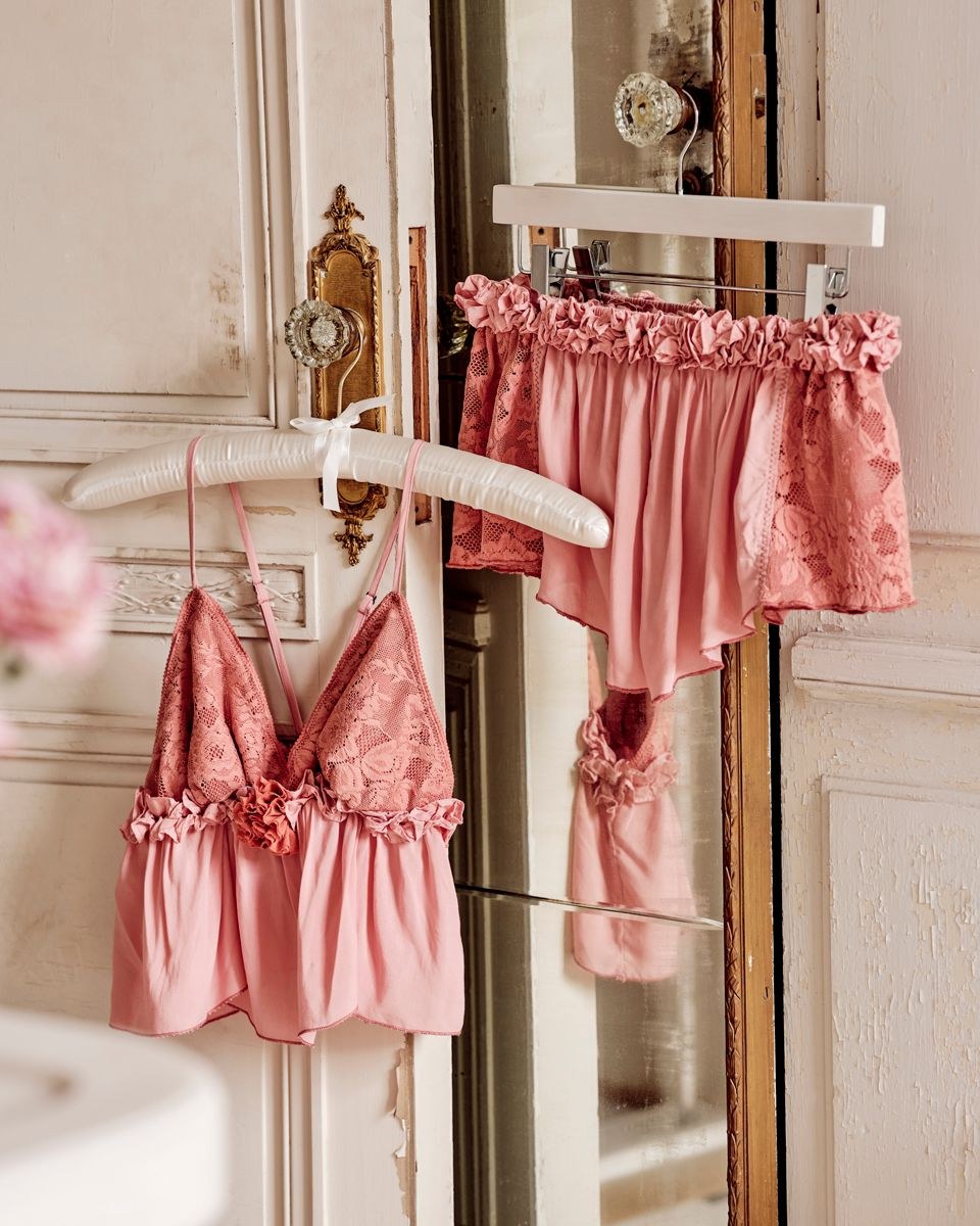 Pink lace lingerie hanging beside an antique mirror in a softly lit interior
