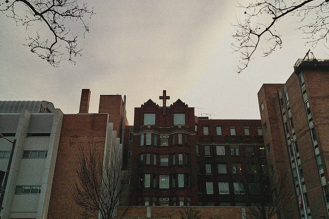 A brick hospital building with a cross beneath an overcast sky, photographed with a Camp Snap camera