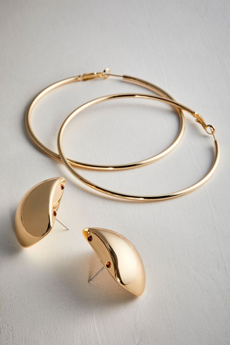 Gold hoop and dome earrings arranged on a pale textured surface