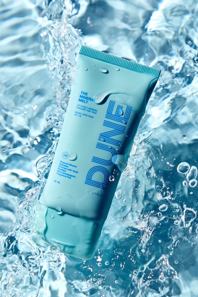 A turquoise skincare tube surrounded by splashing water and droplets