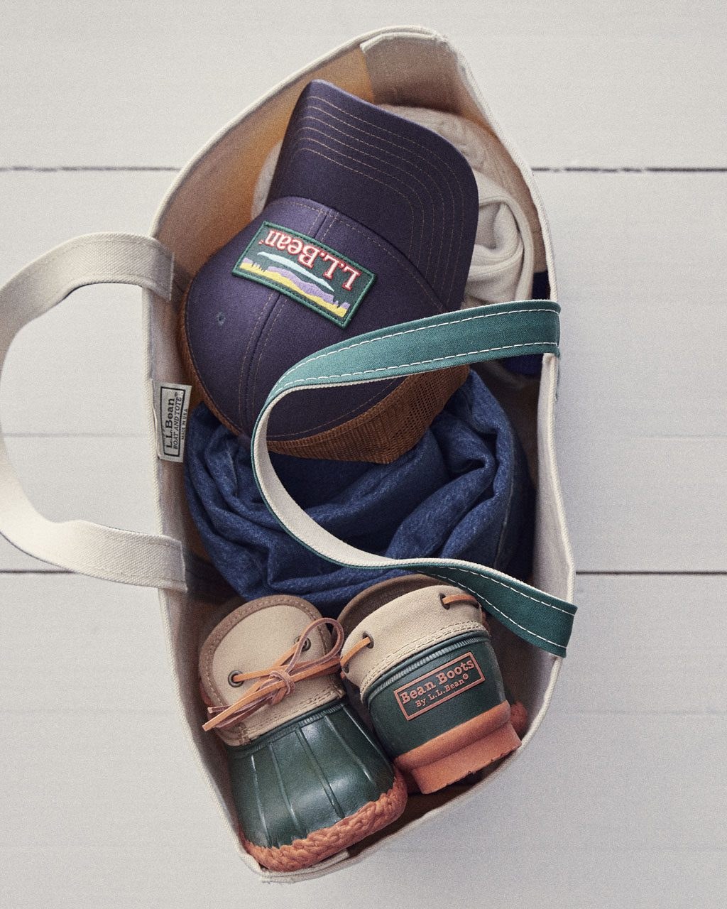 An open canvas tote packed with L.L.Bean hats, clothing, and small duck boots
