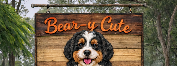 happy Bernedoodle puppies reads "Bear-y Cute BERNEDOODLES", above a smaller sign saying "waiting for our families" in a grassy field