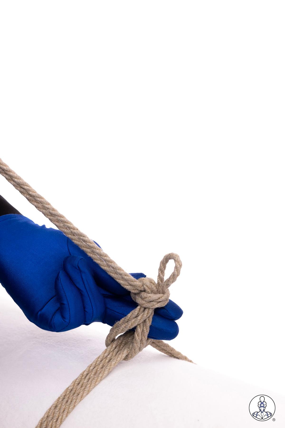 Hand wearing blue glove demonstrates creating a loop in natural jute rope against white background, showing basic rope handling technique with twisted fibers visible in the cordage.