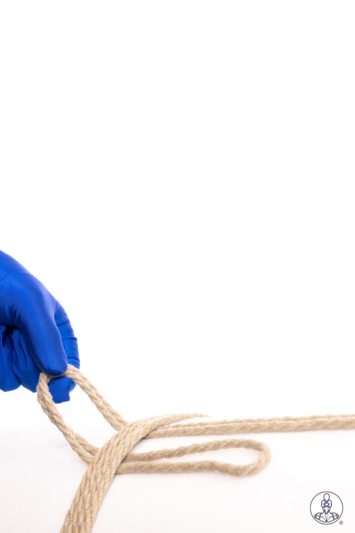 Blue-gloved hand pulling natural jute rope through a partially formed loop, demonstrating a foundational knot-tying technique with beige twisted fiber rope on white background.