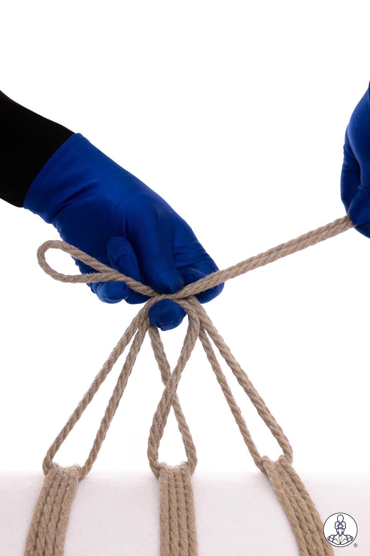 Blue-gloved hands demonstrating rope management technique with natural jute rope, showing how to organize multiple rope strands with loops and a gathering point above the hand against white background.