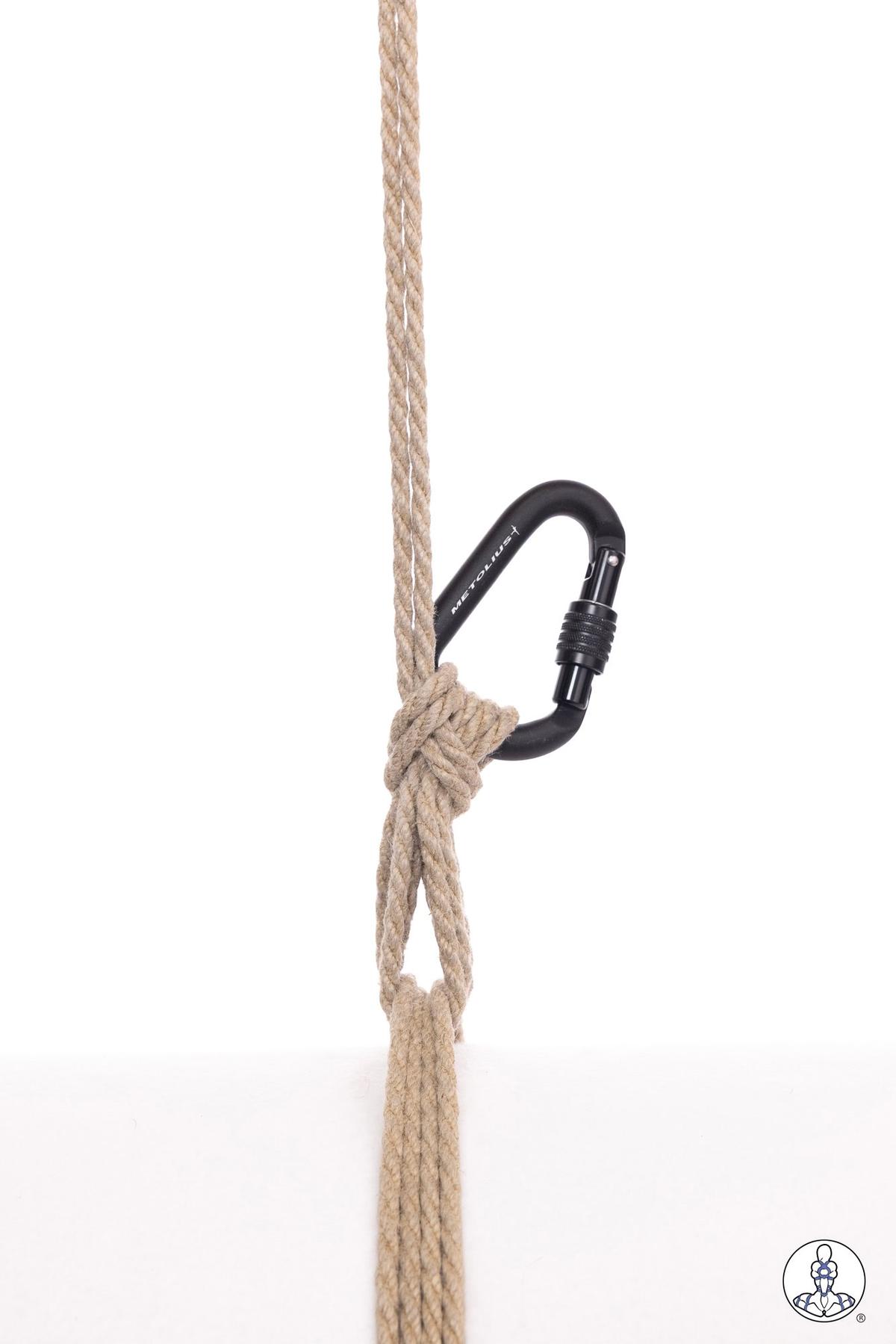 Natural jute rope threaded through a black locking carabiner, demonstrating a basic attachment method with the rope forming a loop and wrapped around the carabiner gate.