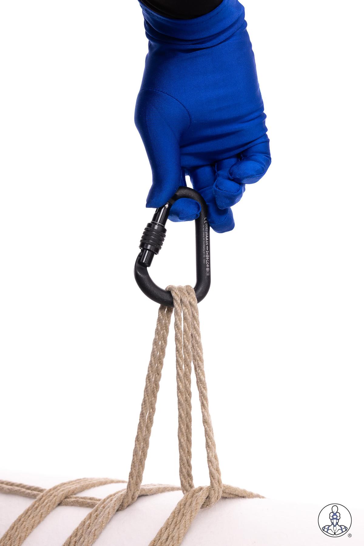 Blue-gloved hand holding a black locking carabiner threaded through four strands of natural jute rope against a white background, demonstrating rope rigging hardware attachment.