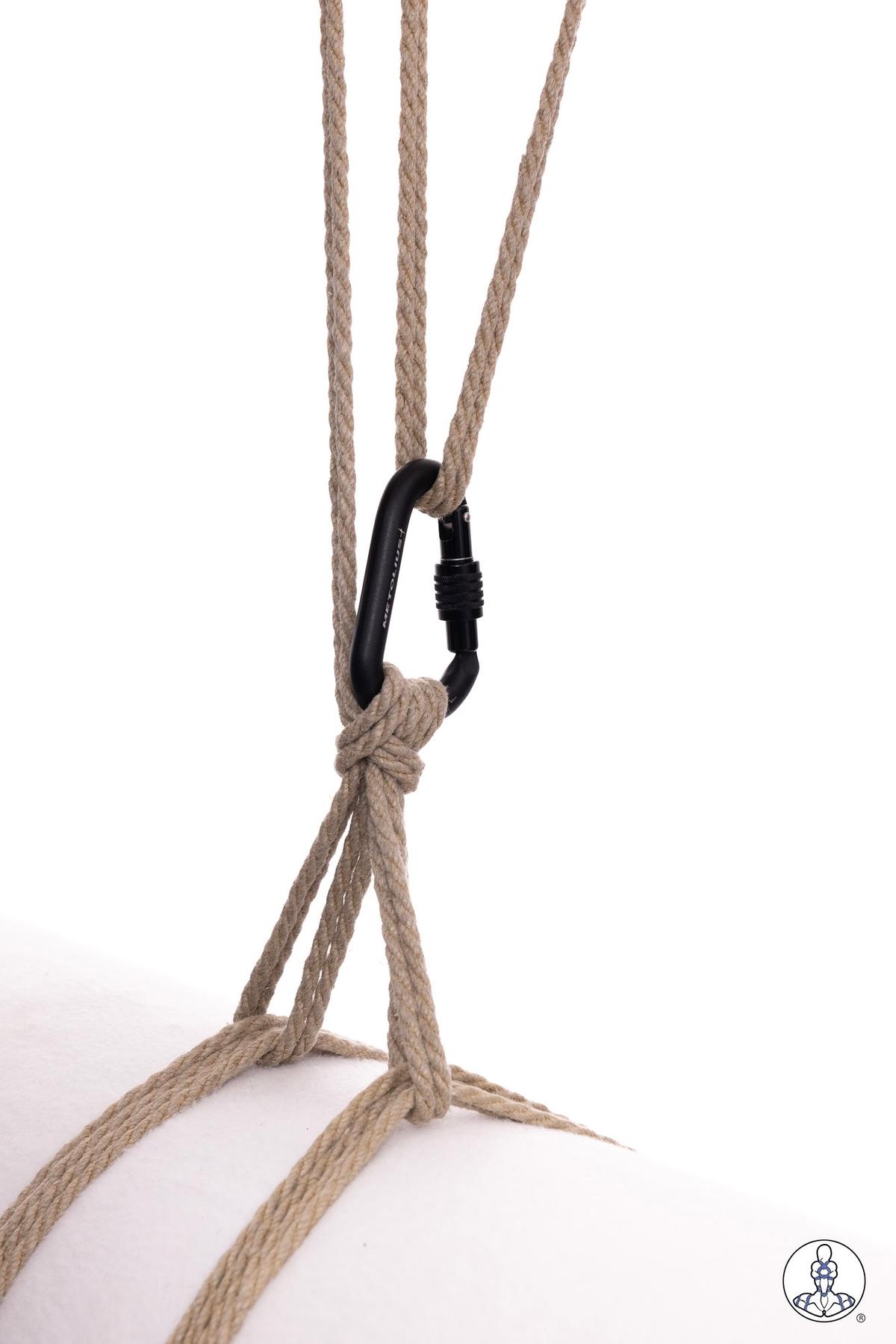 Three strands of natural jute rope secured through a black locking carabiner, demonstrating a suspension point setup with rope gathered and knotted below the carabiner.