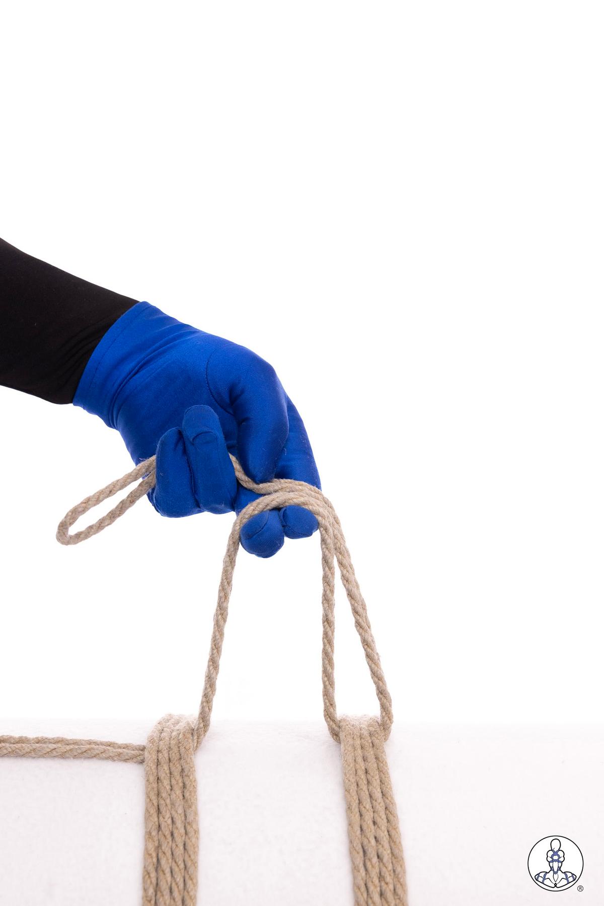 Blue-gloved hand demonstrating rope handling technique with natural jute rope, showing two parallel rope bundles with loops being formed or adjusted above them on white background.