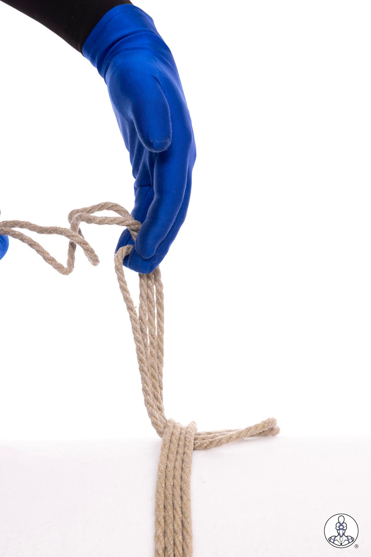 Blue-gloved hands threading natural jute rope through a loop to create a lark's head knot, shown against white background with rope strands hanging downward.