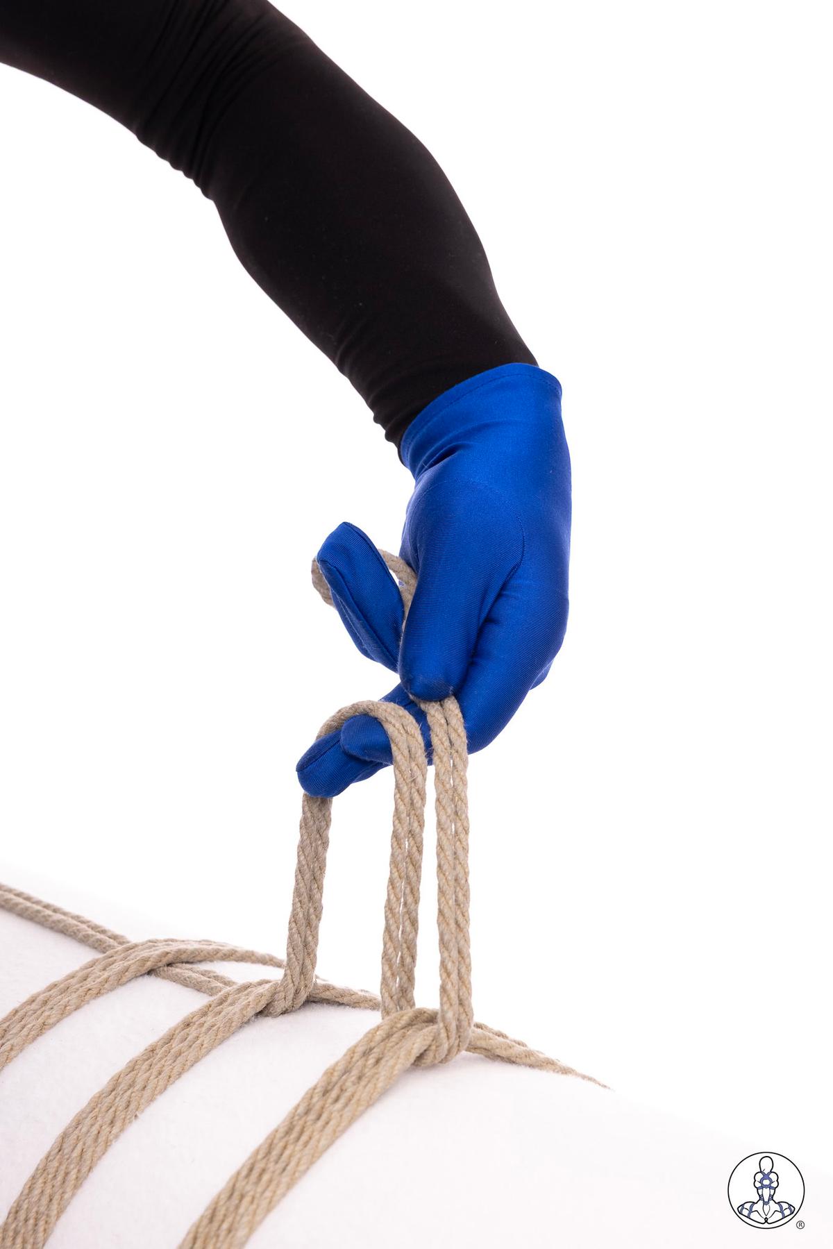 Hand wearing blue fabric glove gripping natural jute rope strands against white background, demonstrating rope handling technique with arm extended downward in black sleeve.