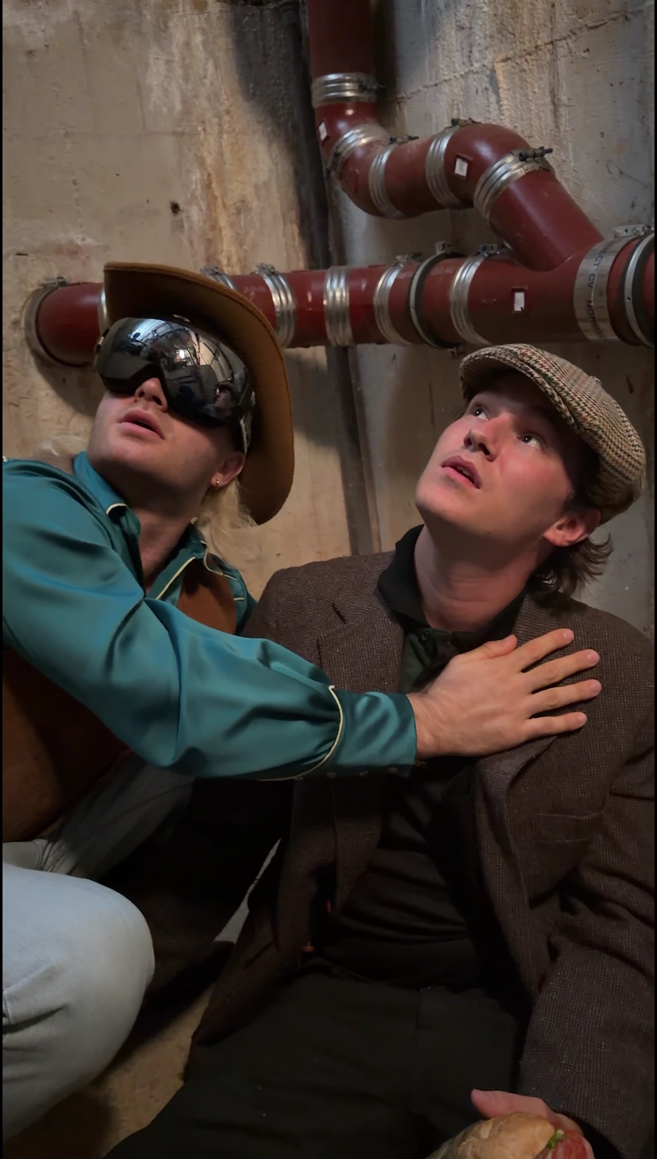 Two characters crouch beneath exposed basement pipes, looking upwards in the Subway campaign.