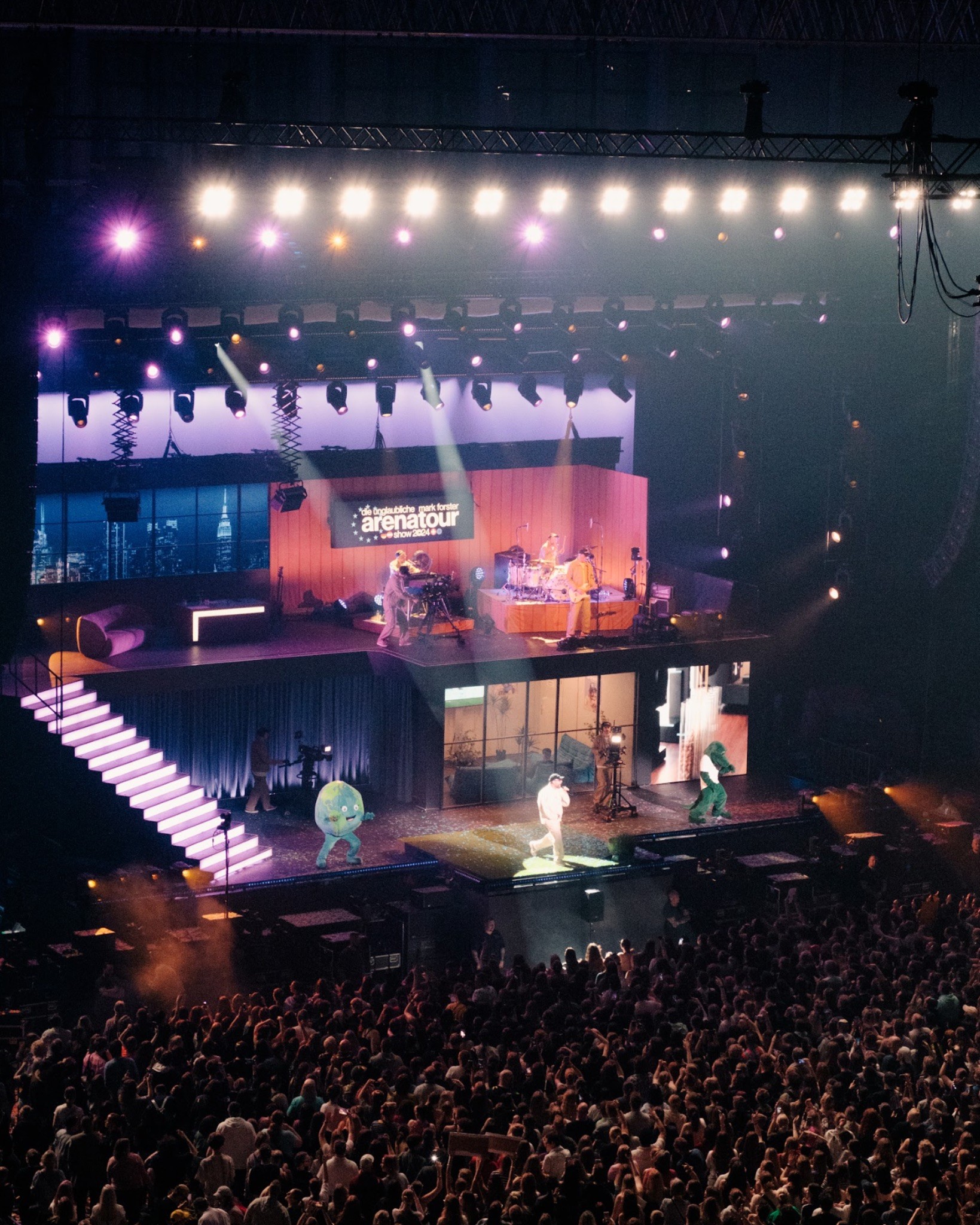 The stage from high up during the show: band on the upper level, a performer on the lower platform and two costumed mascots beside him.