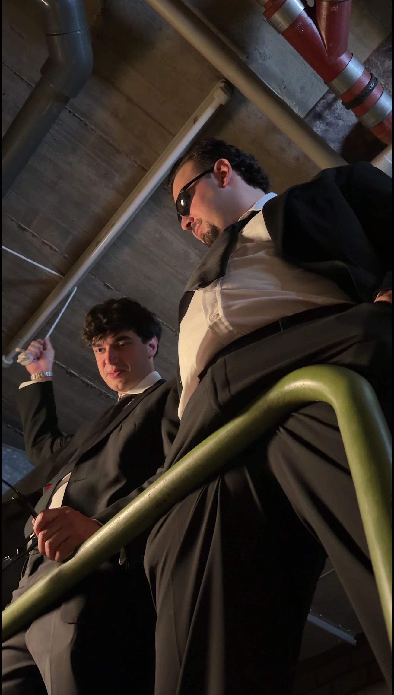 Low-angle Subway campaign still of two characters on a metal staircase beneath exposed pipes.