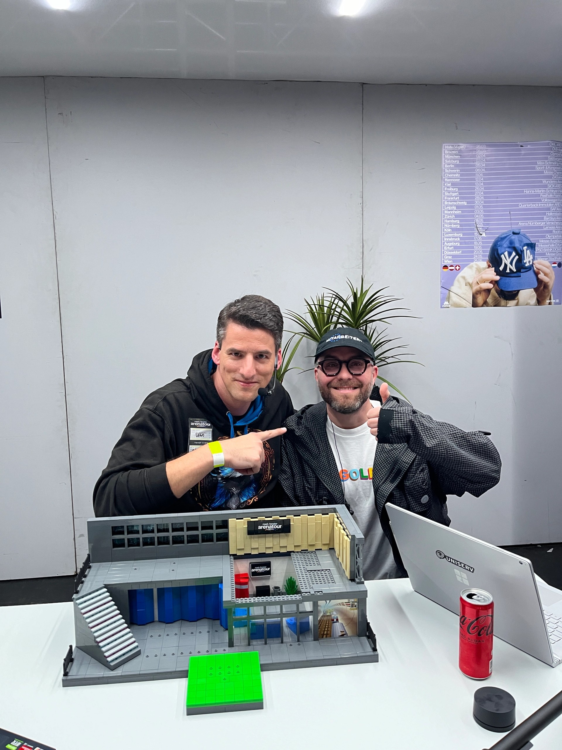 Two people posing behind the completed LEGO arena-stage model on a table.
