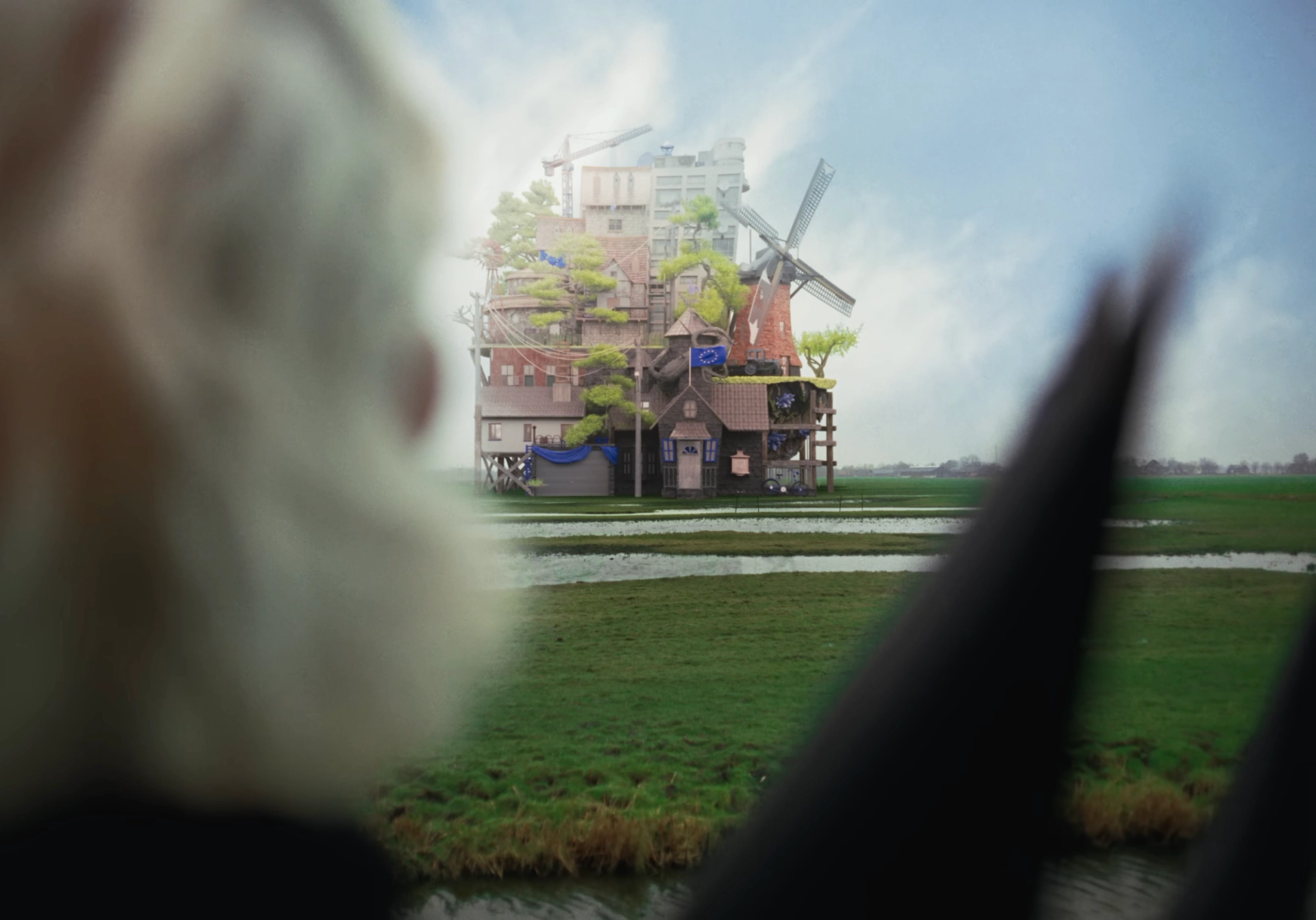 3D house in a flat green polder, seen past a blurred blond figure: stacked Dutch houses, a windmill, a tower block, a crane and an EU flag.