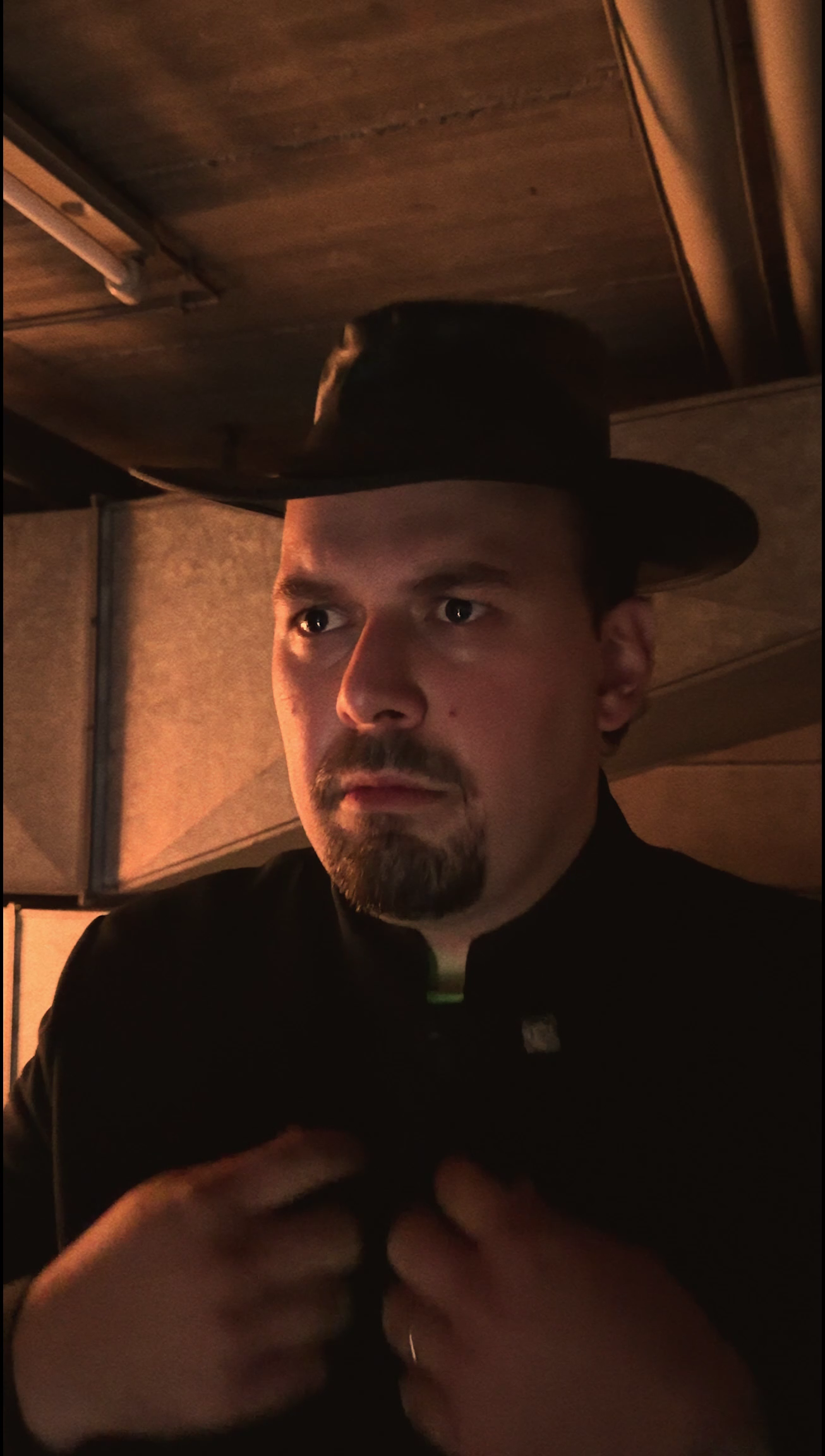 Close-up of a campaign character wearing a black hat and adjusting his collar in a dim wooden interior.