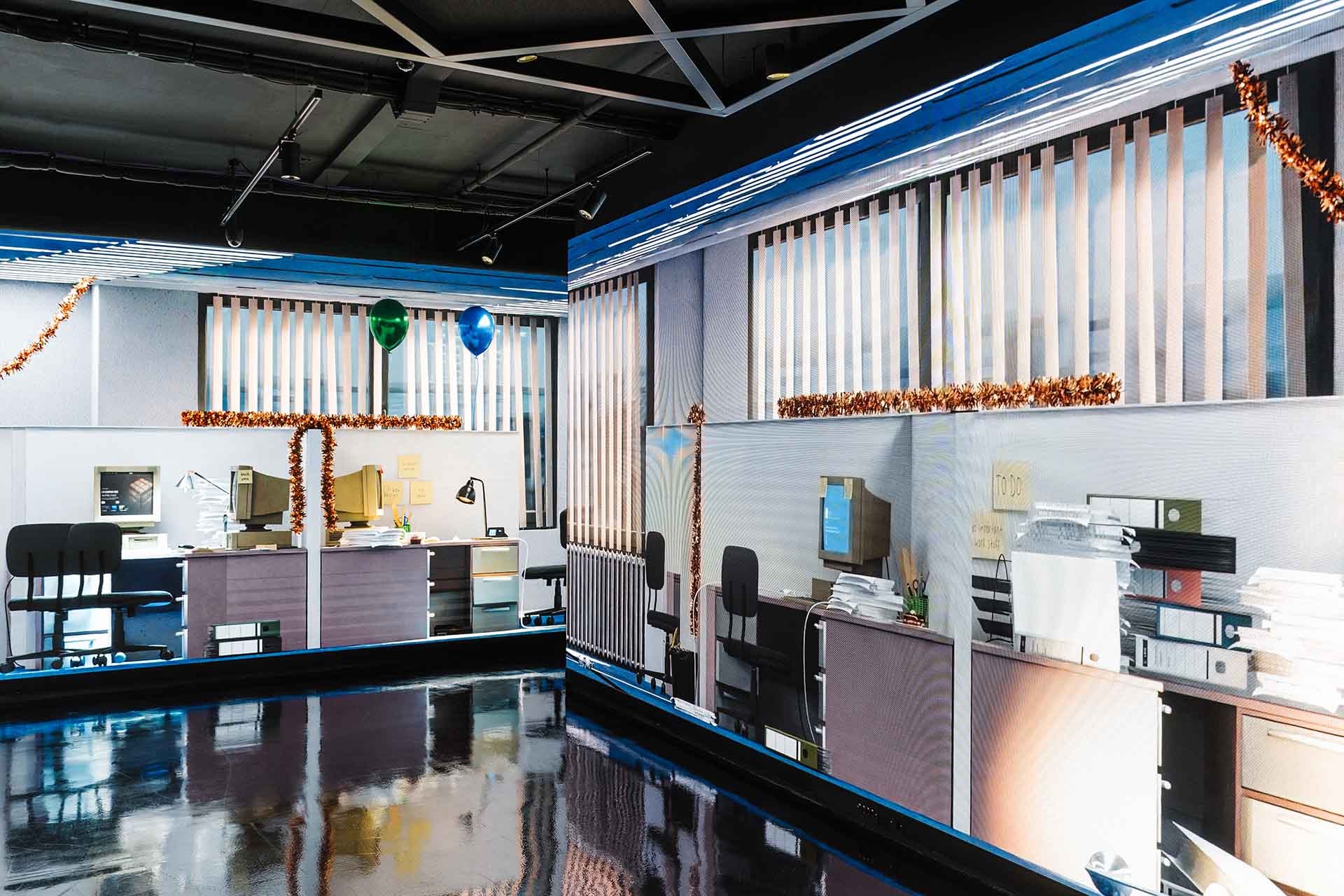 Closer view of the screen walls: desks with CRT computers, sticky notes, ring binders and stacks of paper under copper tinsel, shown at room scale.