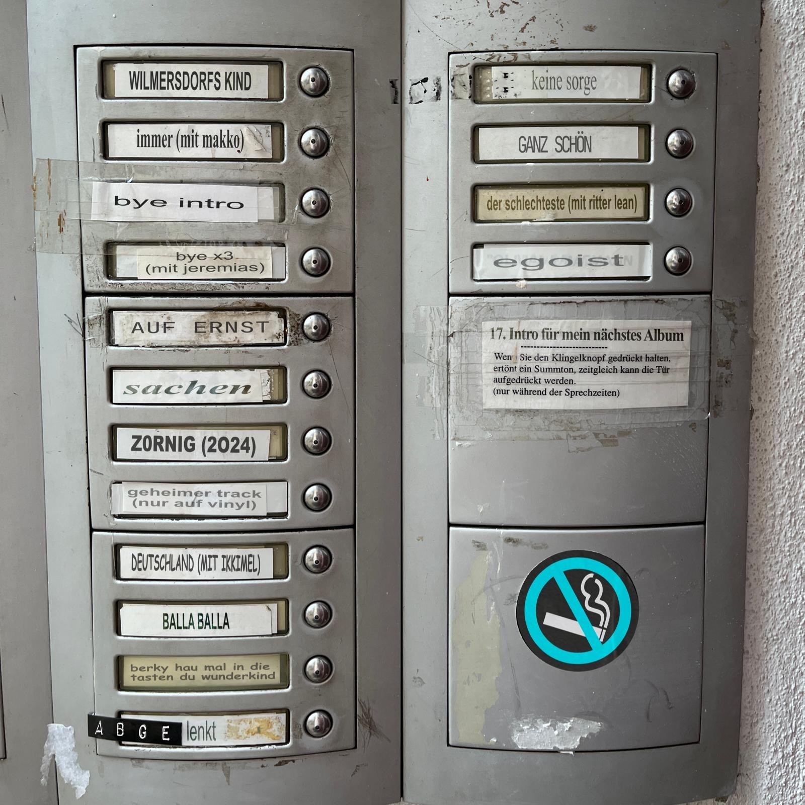 Doorbell panel of an apartment building with the album's track titles as name plates, starting with "WILMERSDORFS KIND" at the top left.