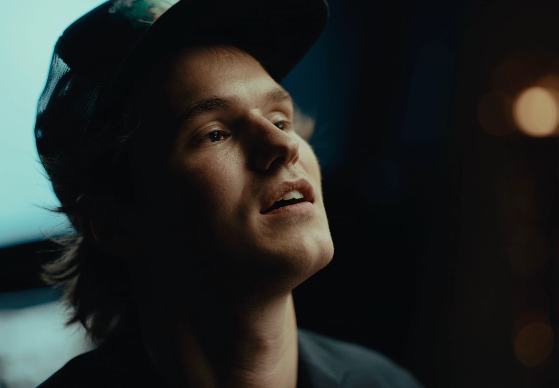 Close-up of Flaschko in the black cap looking up and speaking, his face half in shadow against blurred lights.
