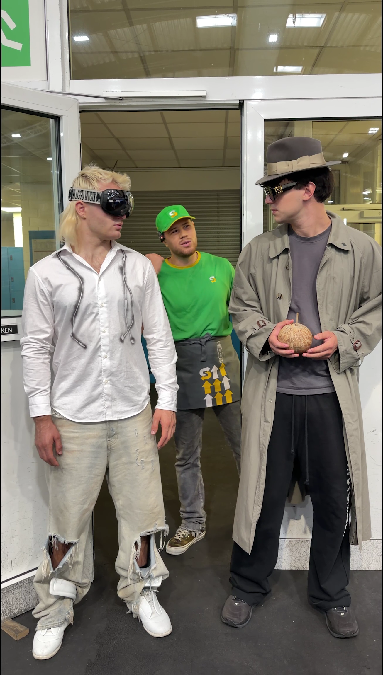 Two visitors in sunglasses stand with a Subway employee in green at the restaurant entrance.