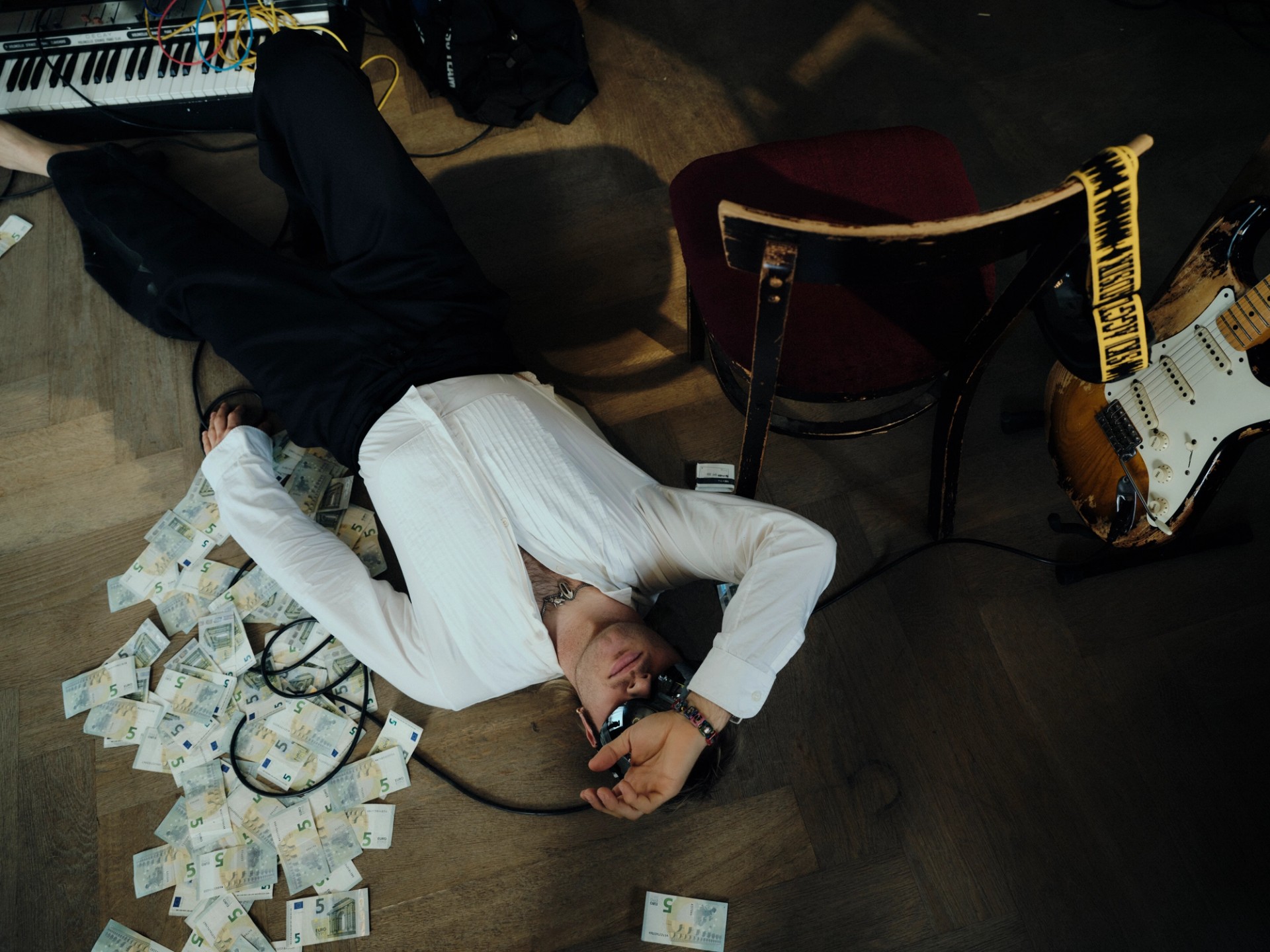 Overhead view of a performer lying beside a chair, guitar, cables and scattered banknotes on the SkiAgguMusik set.