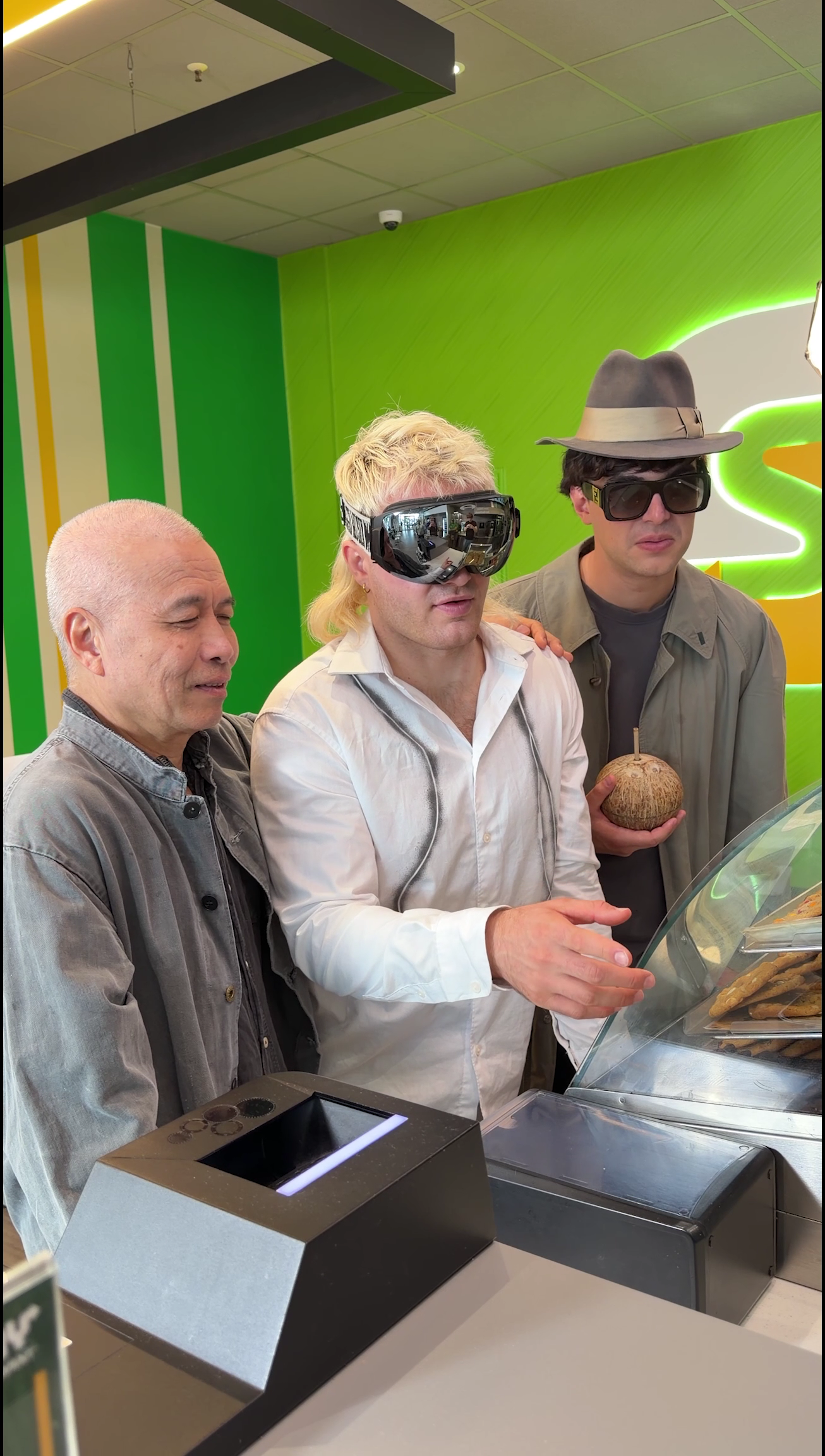 Three people at a Subway counter, including a visitor wearing mirrored goggles and another in a hat.
