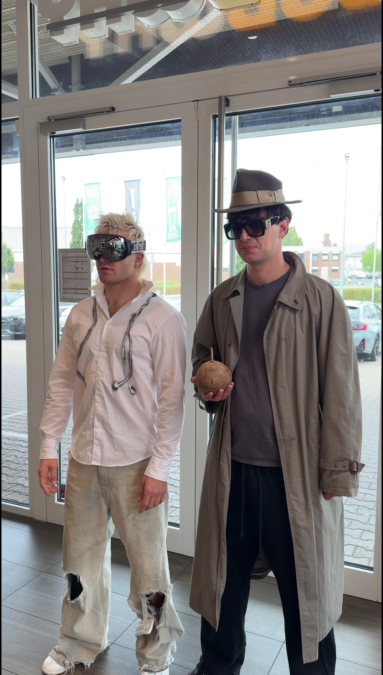 Two campaign characters, one wearing goggles and one in a hat and trench coat, stand inside a Subway entrance.