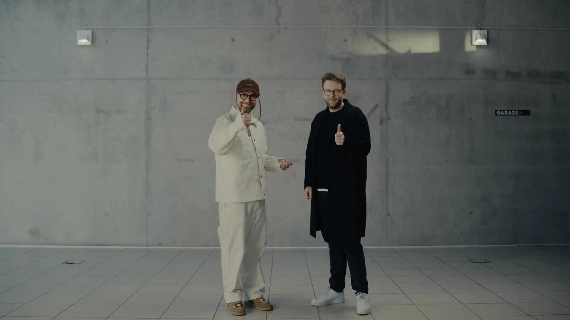 Mark Forster on the left in white and Jakob Lundt on the right in black, standing in a bare concrete room in the Schwarzer Toyota music video.