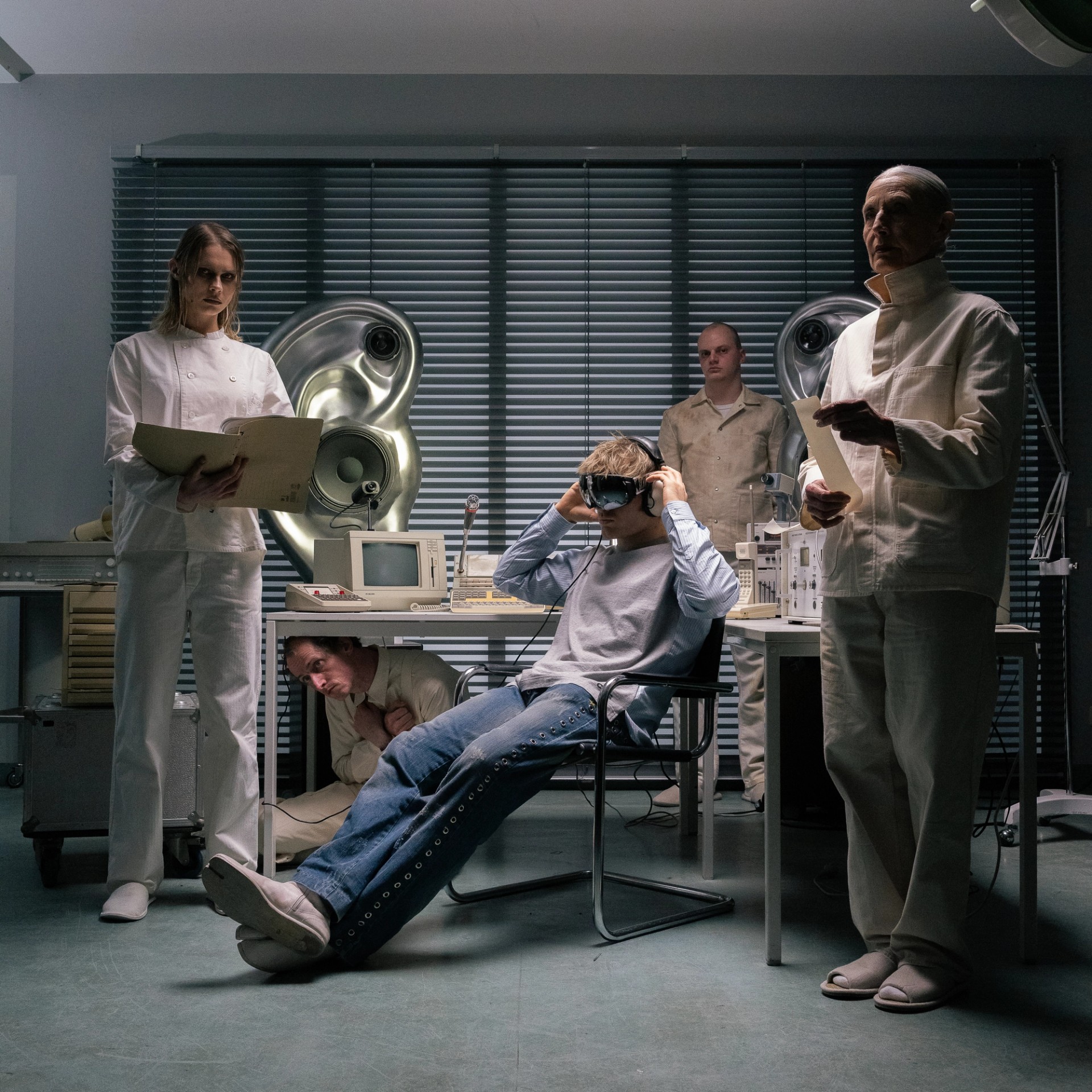 SkiAgguMusik campaign portrait staged as a clinical examination, with a seated goggled performer and three white-clad figures.