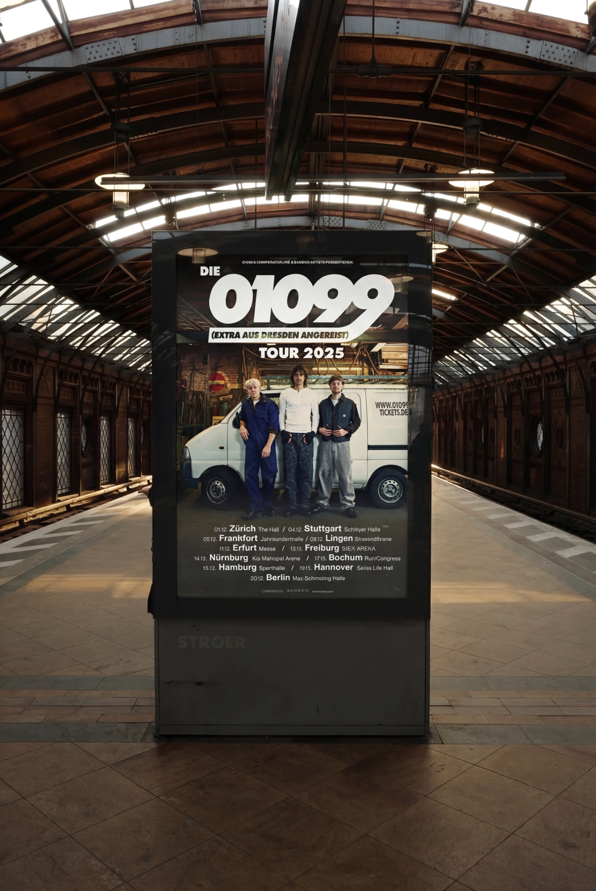The 2025 tour poster in a backlit advertising column on a train station platform.