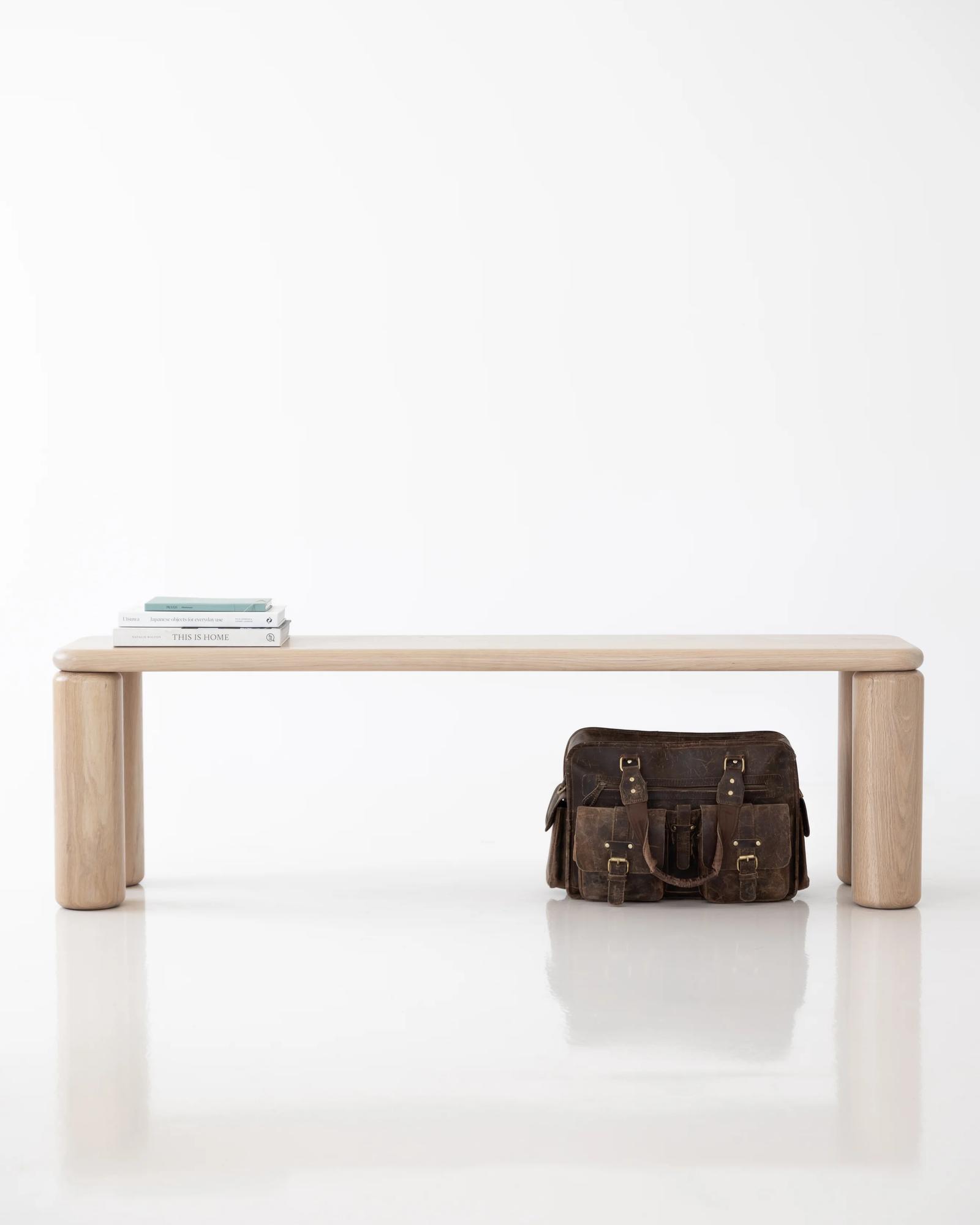Ladovi bench seat in natural oak, front elevation of the long soft-cornered top floating on four chunky rounded cylindrical legs