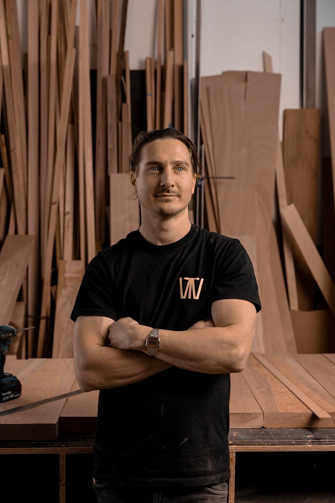 Heath Polkinghorne, founder of Timberwolf Design, in the Henley Beach workshop in front of stacked timber boards.