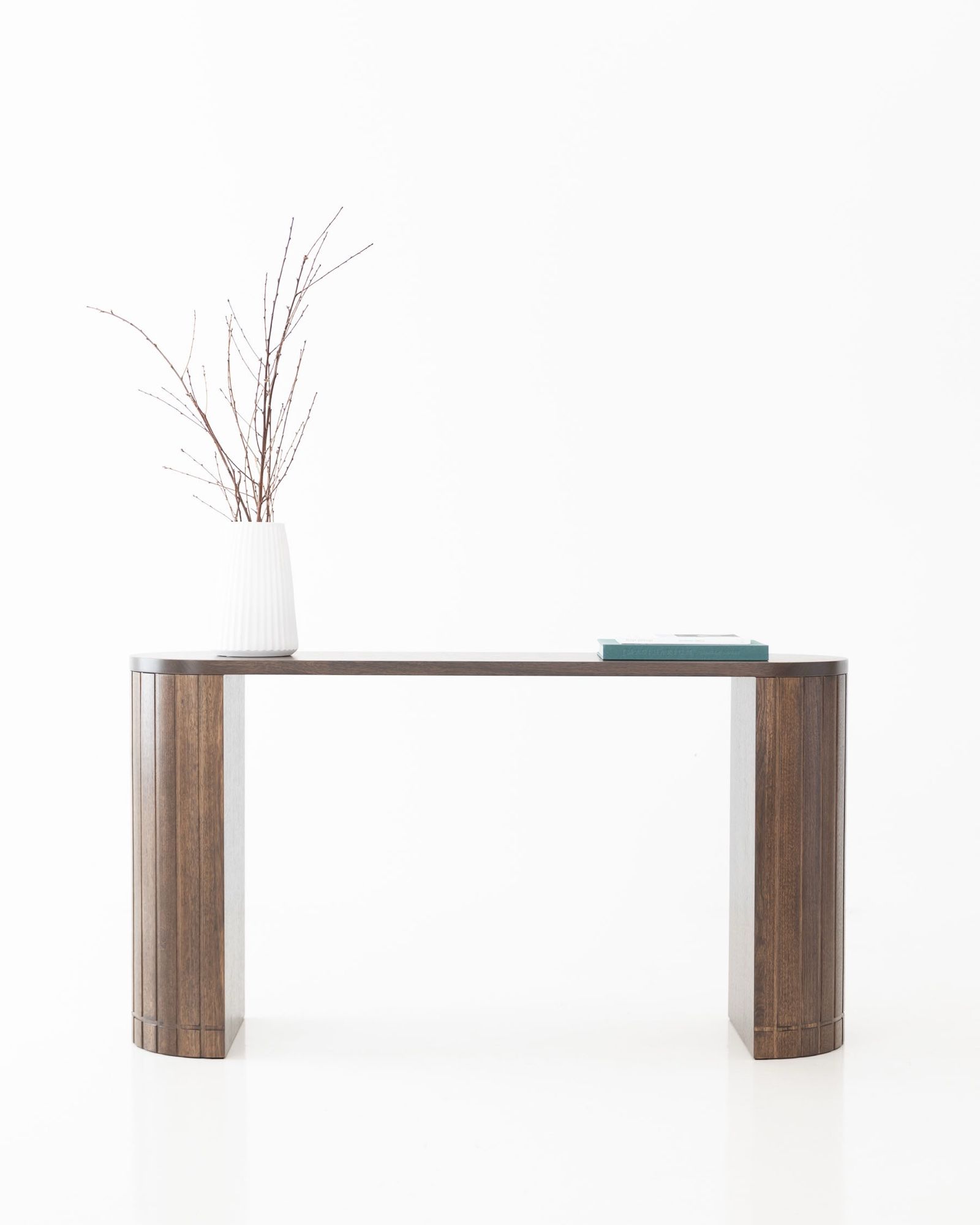 Apolune console table styled with a ceramic vase and dried branches, long horizontal form on pale studio floor