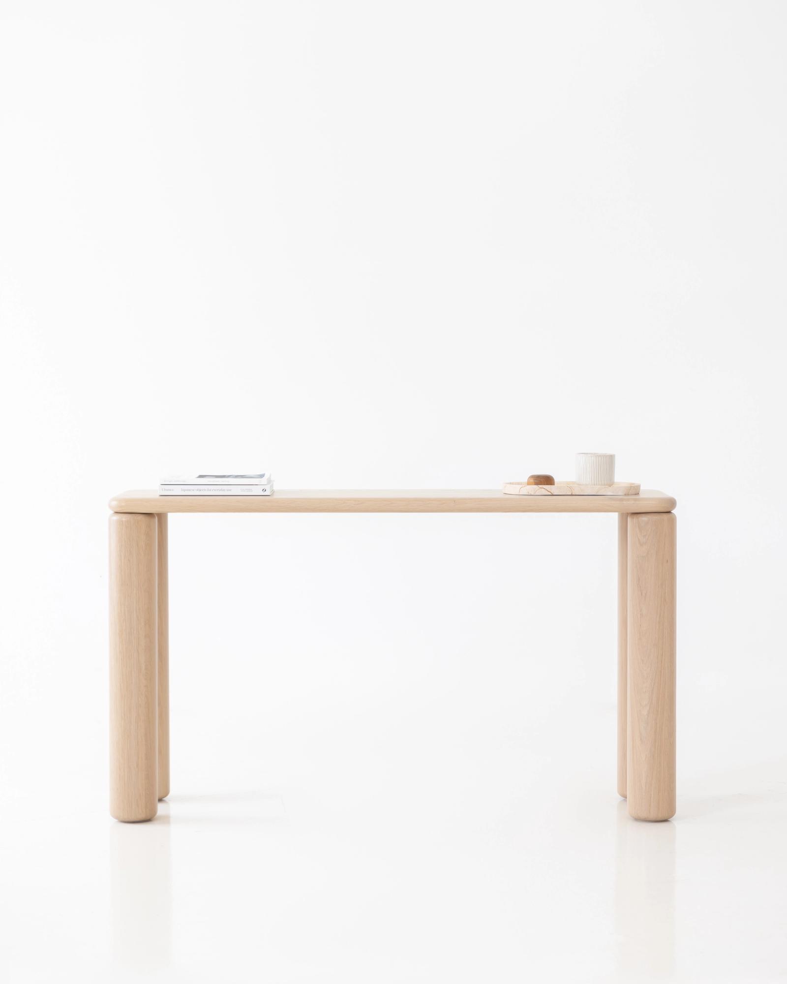 Ladovi hall table in natural oak, three-quarter studio view of the slim console floating on four chunky rounded cylindrical legs