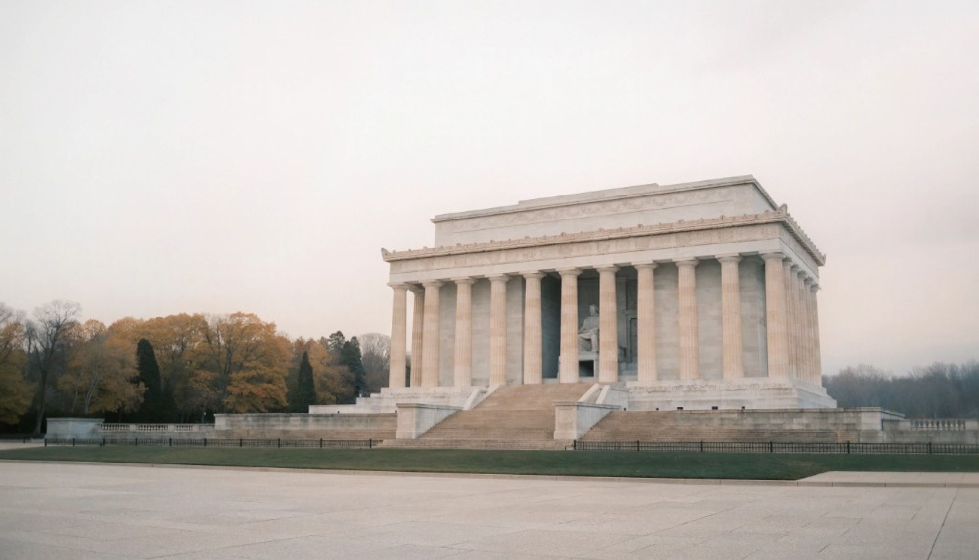 The marble colonnade of the Lincoln Memorial, with the seated statue of Lincoln inside and autumn trees to the left